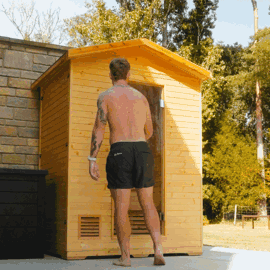 Person entering a small wooden sauna outdoors.