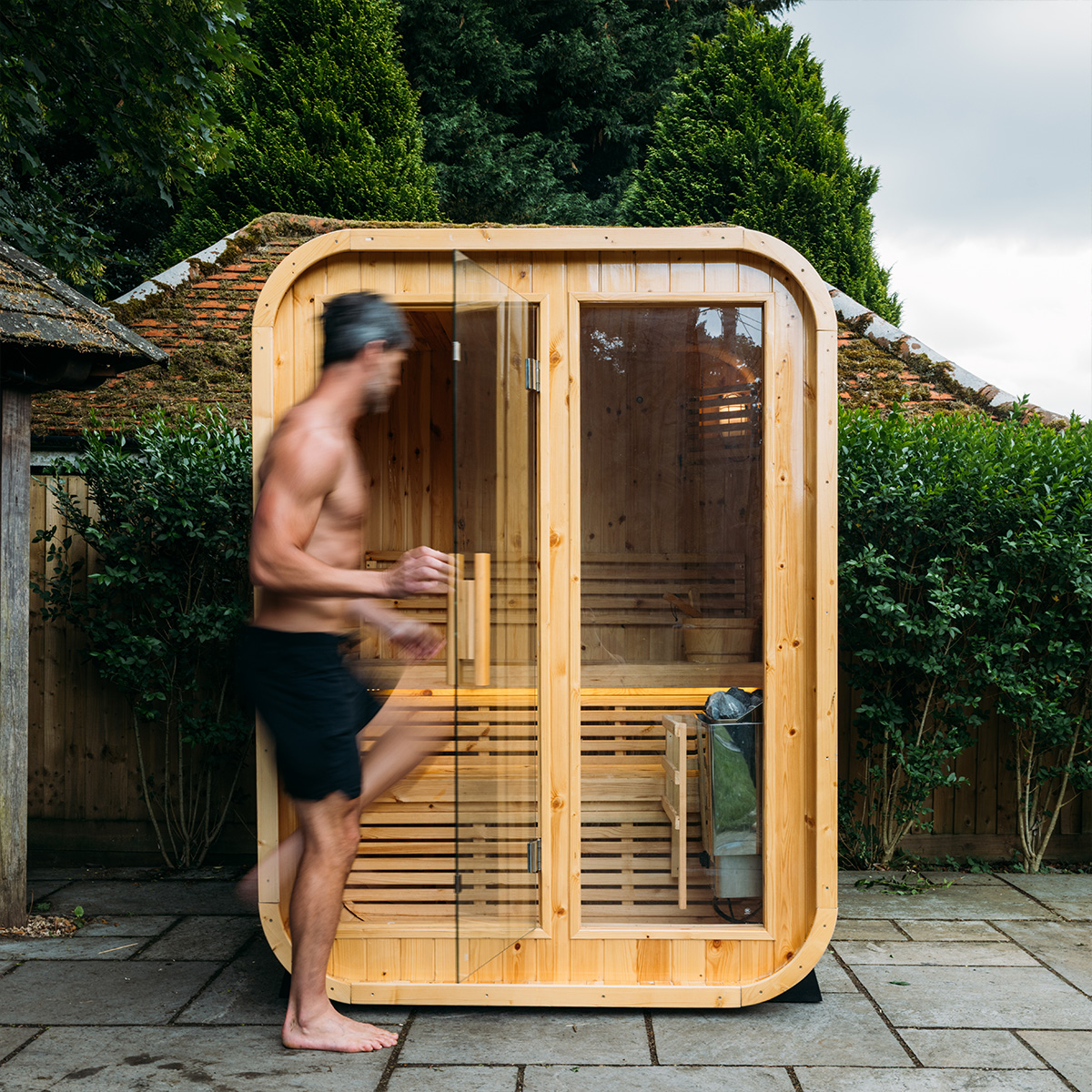 Man entering a small wooden outdoor sauna with glass door.