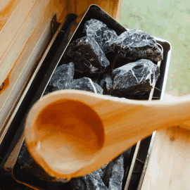 Wooden ladle pouring water over hot sauna stones.
