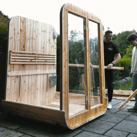 Two people assembling a wooden structure with glass panels outdoors.