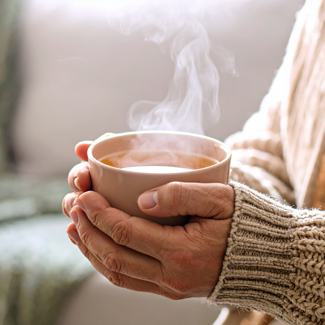 A close-up of a person's hands in a chunky knit sweater holding a steaming mug.