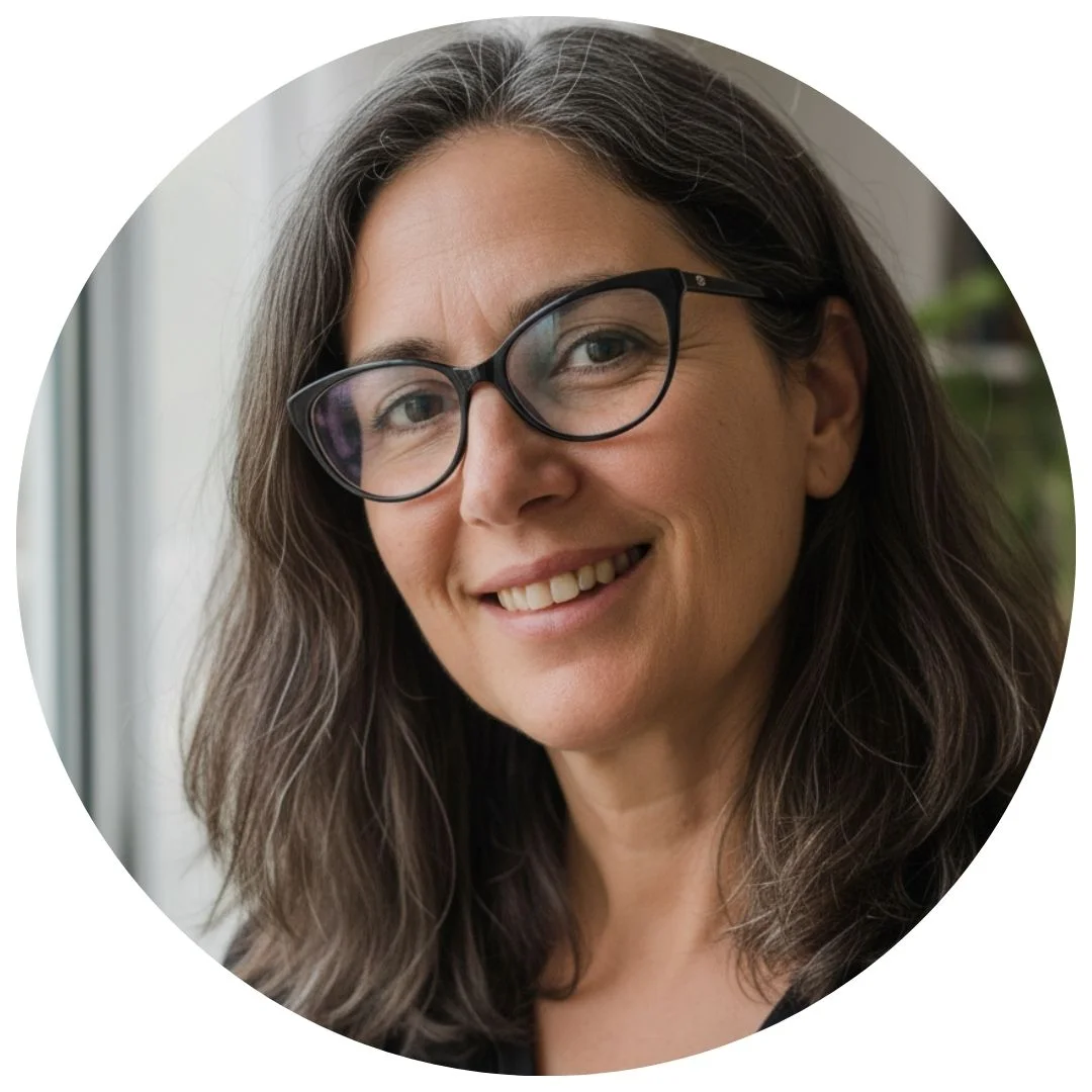Smiling person with glasses and long hair near a window.