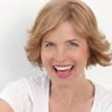 Smiling person with short, light hair wearing a white shirt against a plain background.