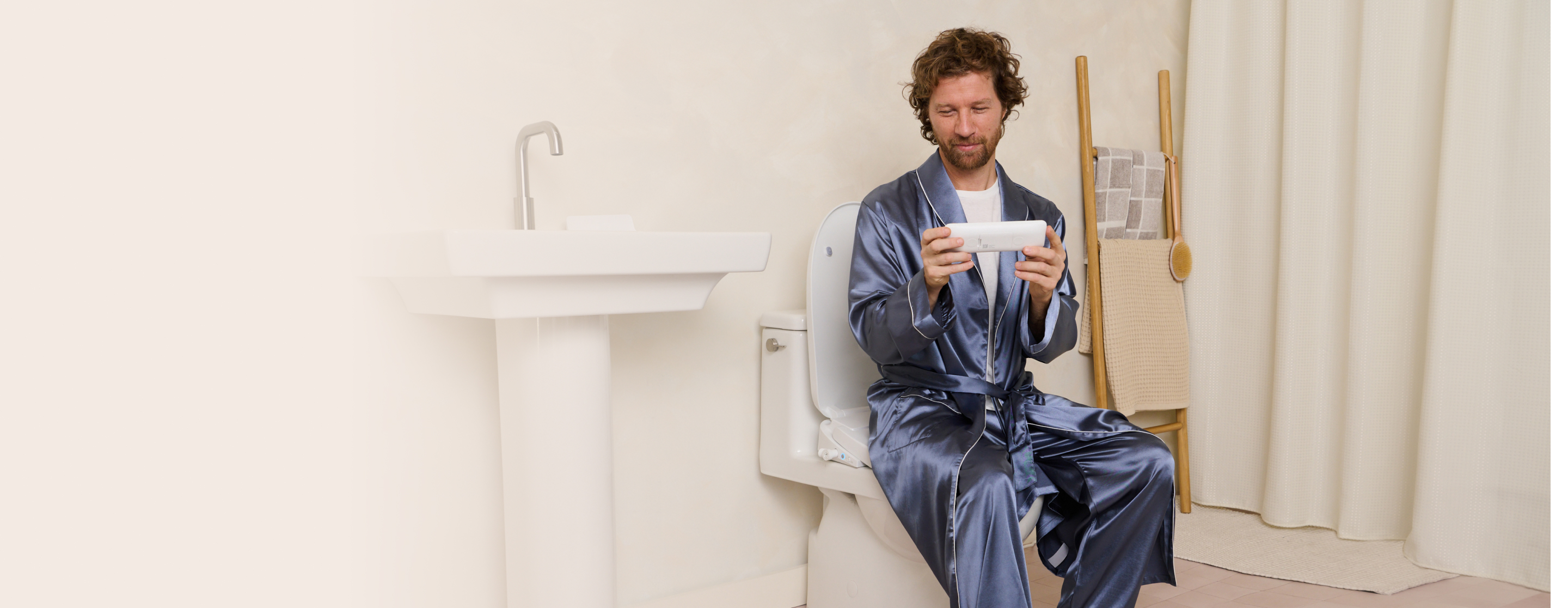 Person in a blue robe sitting on a toilet, holding a device.