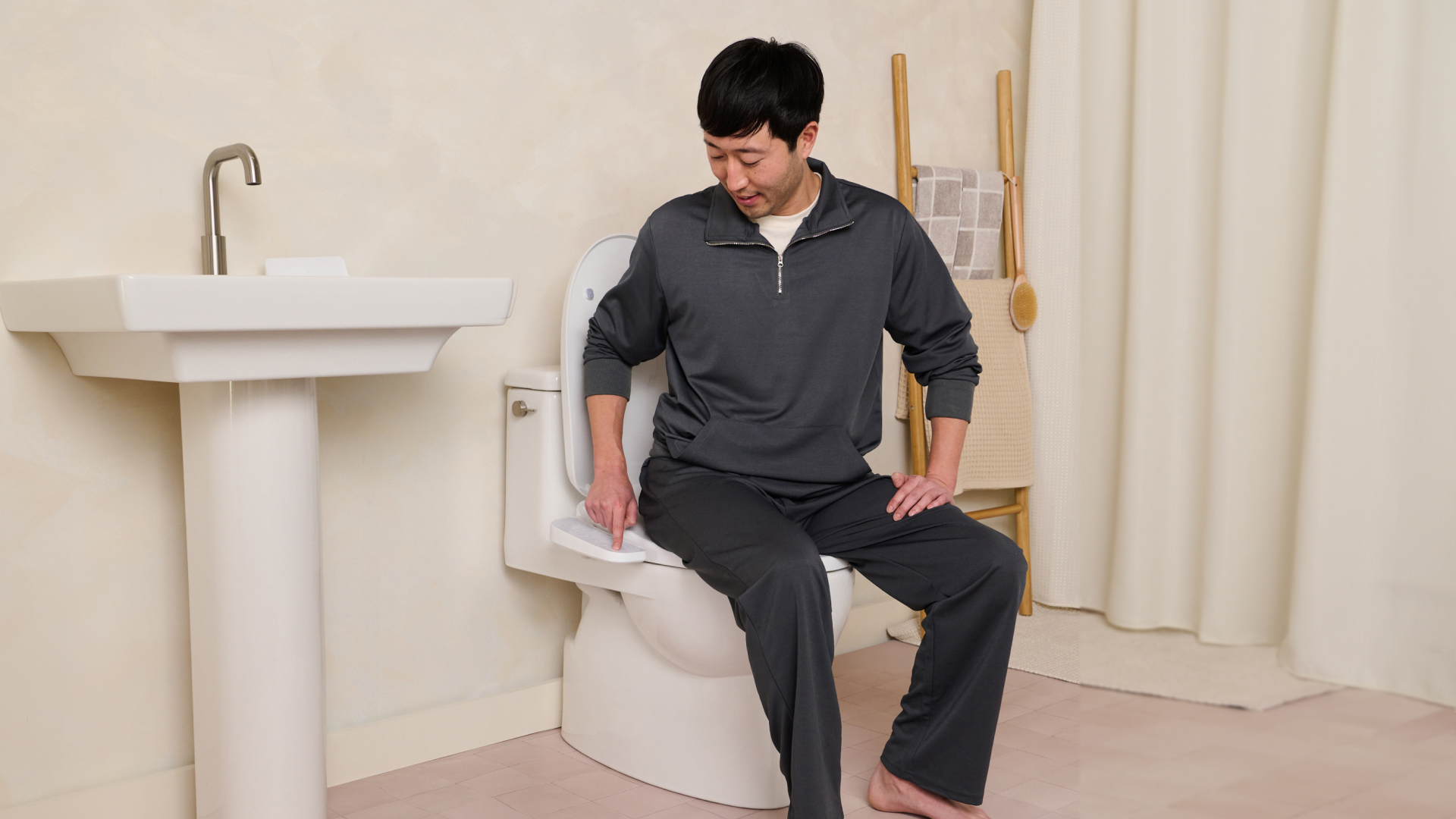 Person sitting on a toilet, pointing at a control panel.