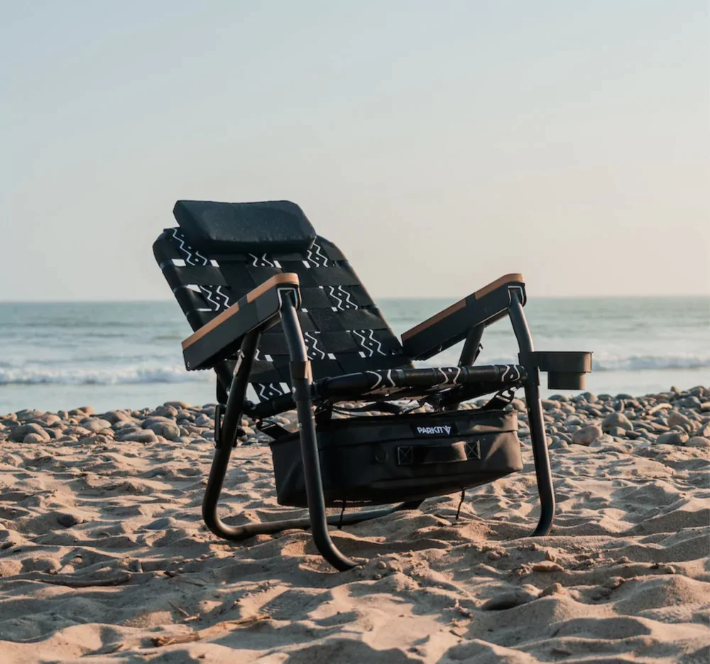 Lounge chair on a sandy beach with ocean waves in the background.