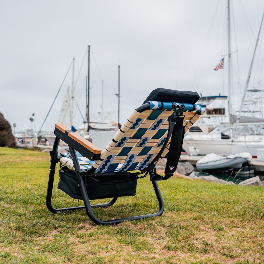 A patterned lawn chair sits on a grassy hill overlooking a marina filled with boats.