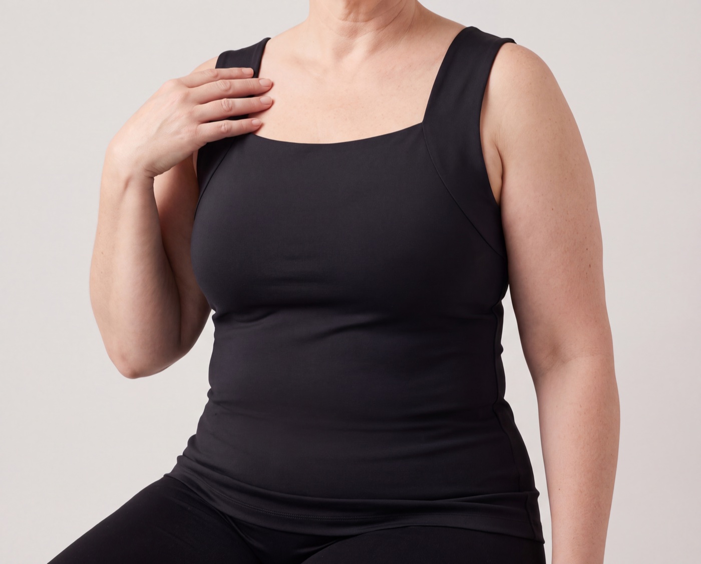Woman wearing the black tank with built-in cups, hand resting on the wide strap