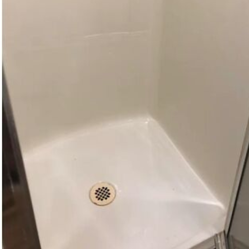 Empty white shower stall with a drain.