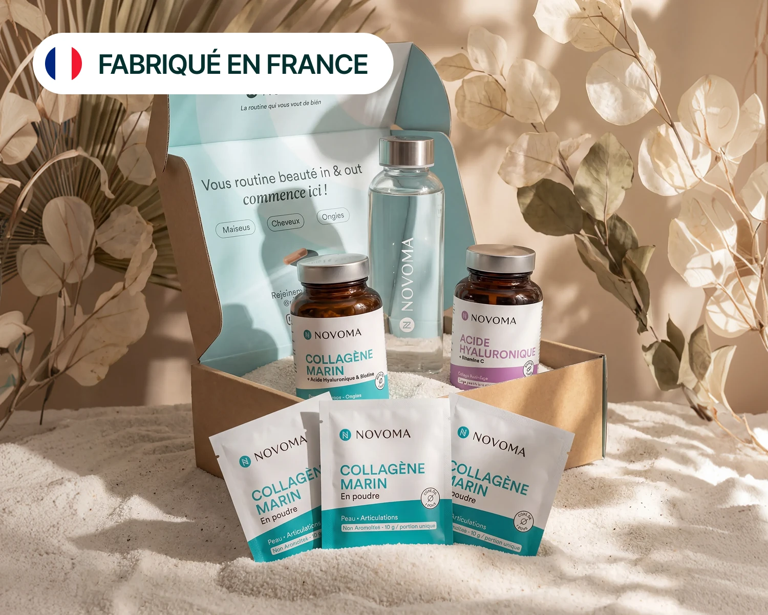 An open box of Novoma beauty products, including collagen and hyaluronic acid, on a bed of sand.