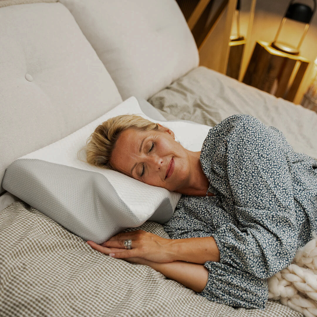 Woman sleeping on a bed with a white ergonomic pillow.