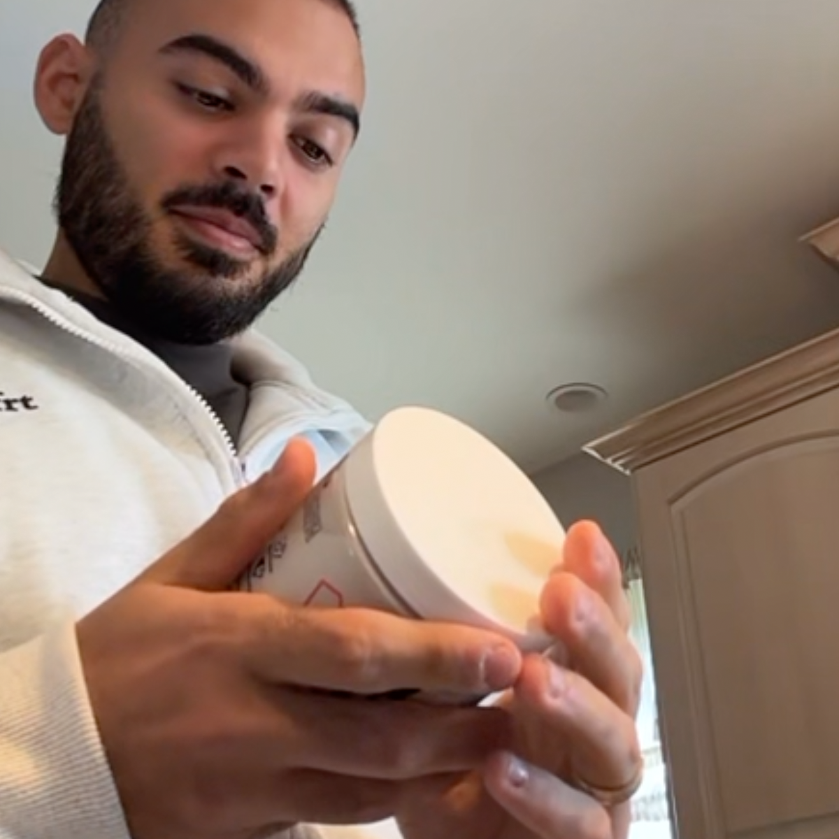 Man in a white jacket examining a container in a kitchen.
