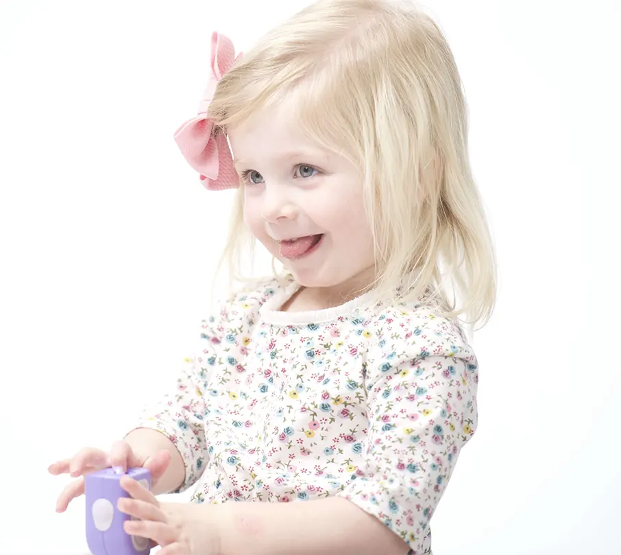 Young child with a pink bow, smiling and playing with a purple toy.