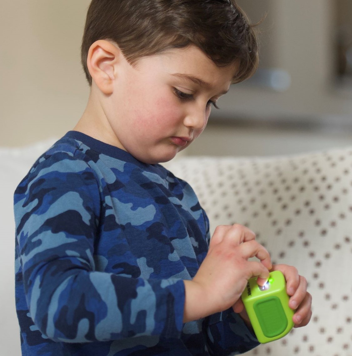 Child in blue camo shirt holding a small green device.