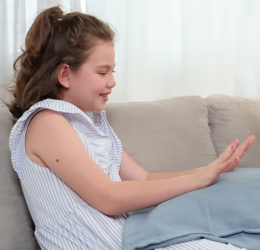 Girl in striped dress smiling, touching a blue pillow on a couch.