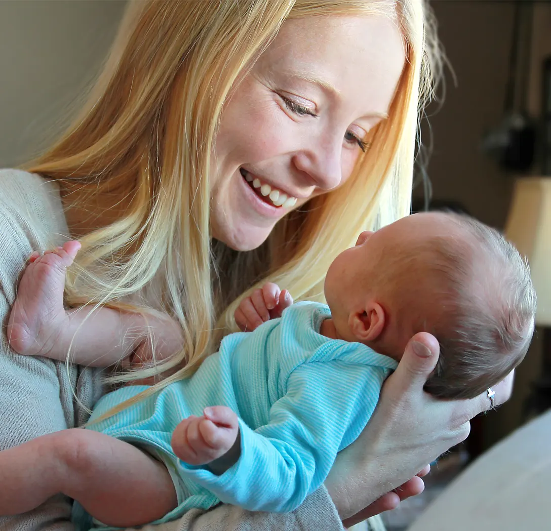 Smiling woman holding a baby in a blue outfit.