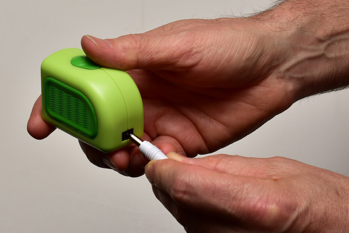 A person connecting a cable to a small green device.