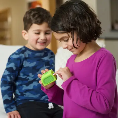 Two children playing with a small green toy indoors.
