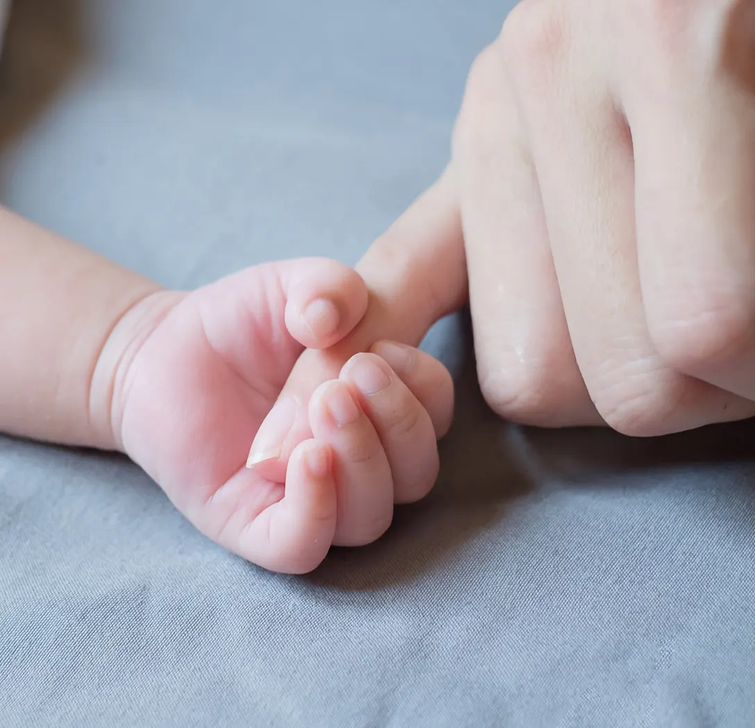 Baby's hand holding an adult's finger on a gray surface.