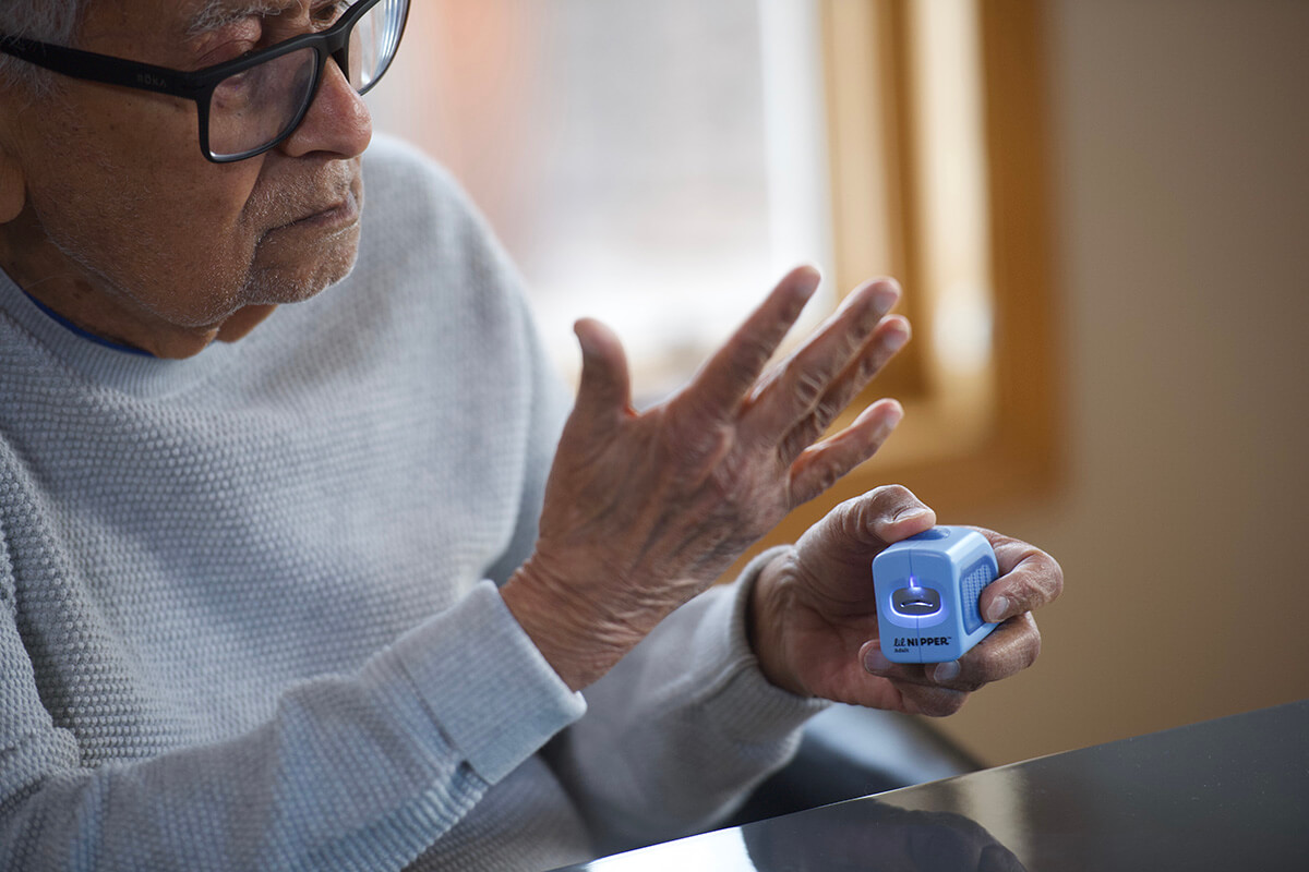 Elderly person using a small blue nail care device.