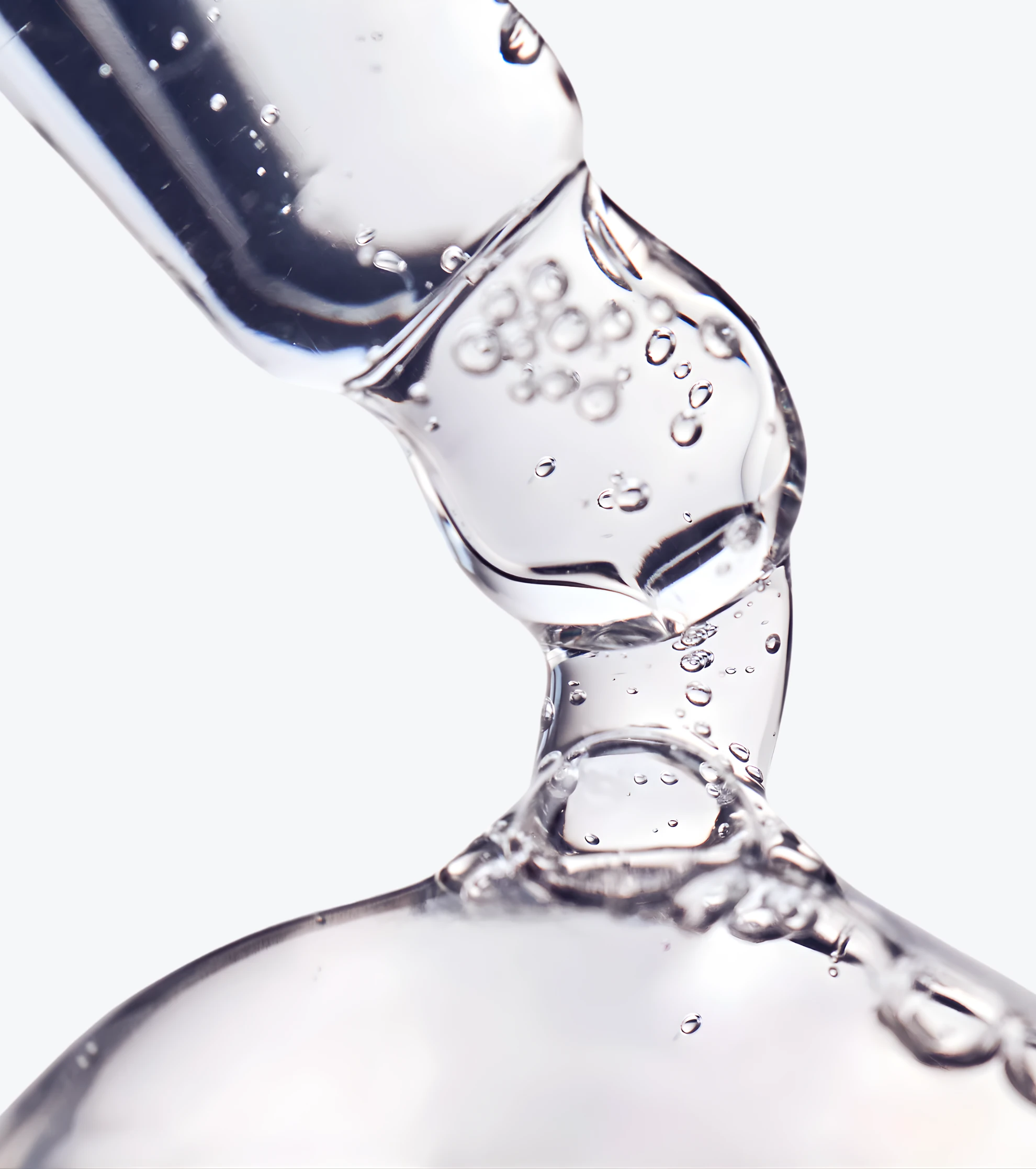 A close-up of a clear, viscous liquid with bubbles being dispensed from a glass dropper.