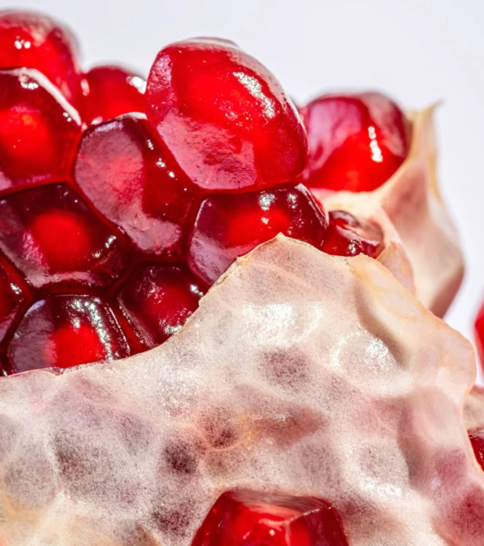 A macro photograph of bright red pomegranate seeds nestled within the fruit's white membrane.