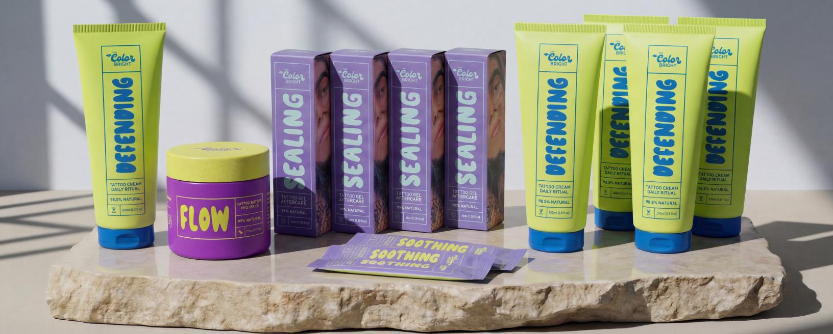 A collection of brightly colored tattoo aftercare products from The Color Bright brand arranged on a stone slab.