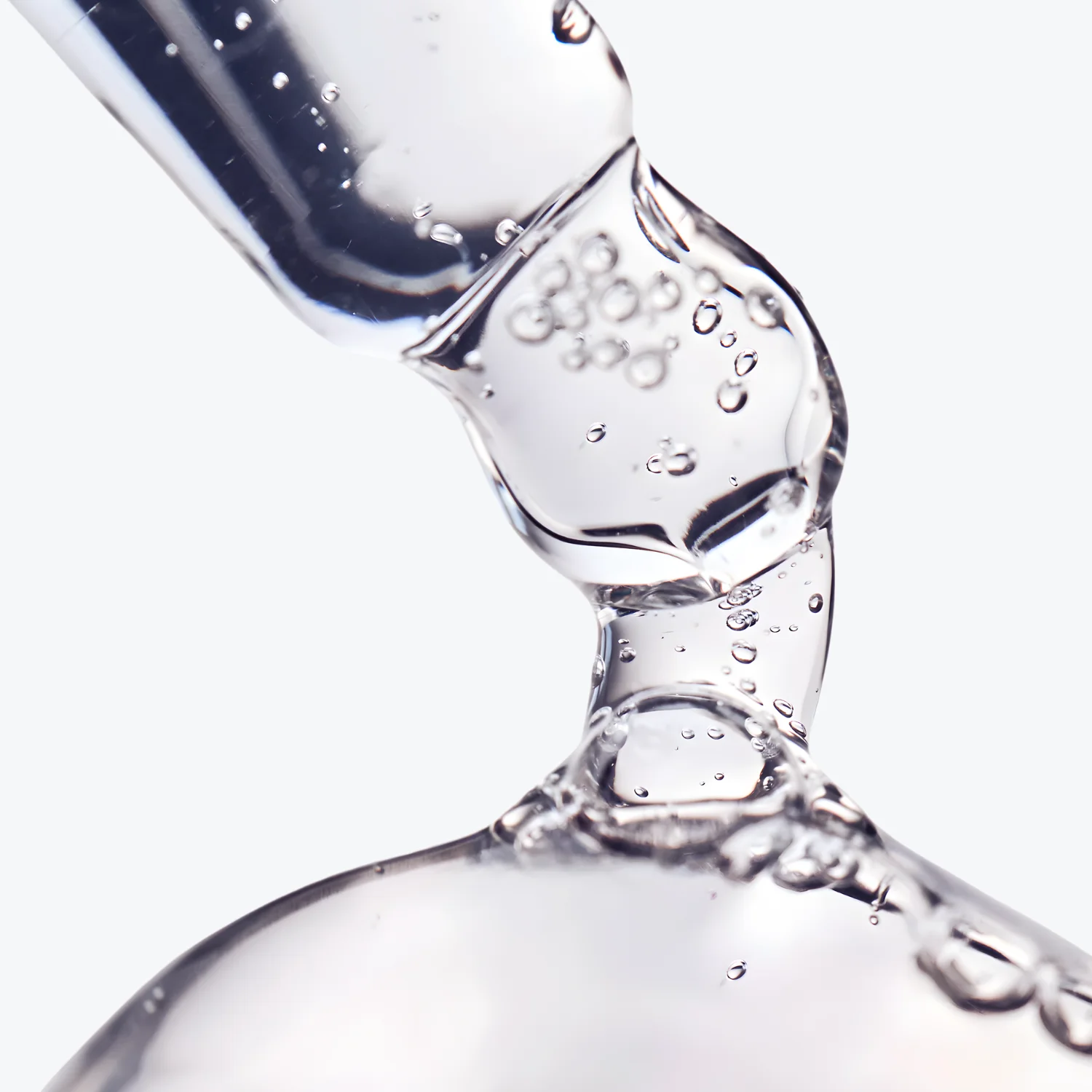 A close-up of a clear, viscous liquid with bubbles being dispensed from a glass dropper.