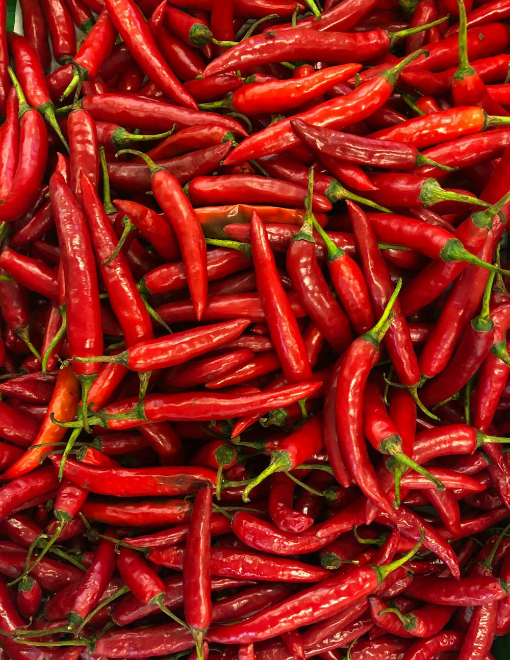 A pile of fresh red chili peppers with green stems.