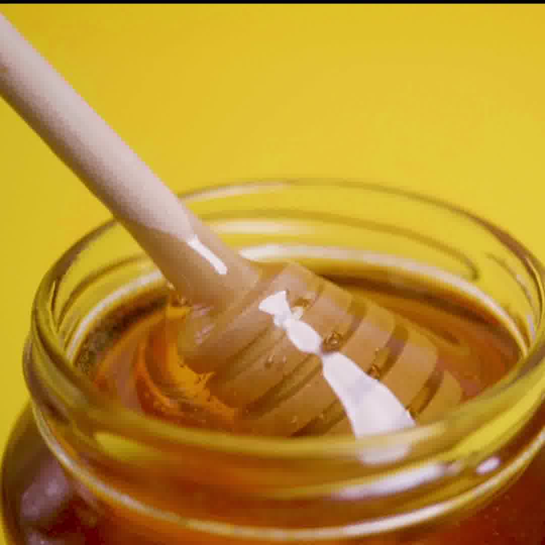 Honey dipper in a jar of honey against a yellow background.