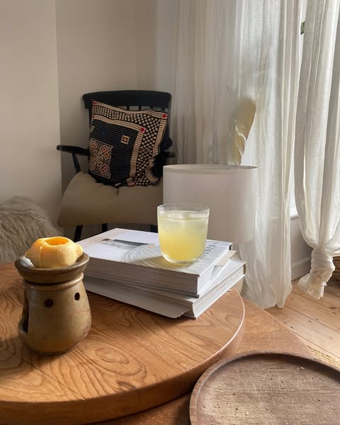 Cozy room with a chair, cushion, books, and a drink on a wooden table.