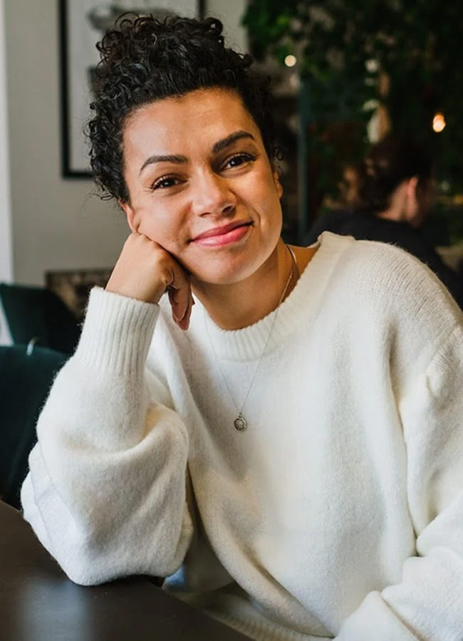 Person in a white sweater smiling, sitting indoors.