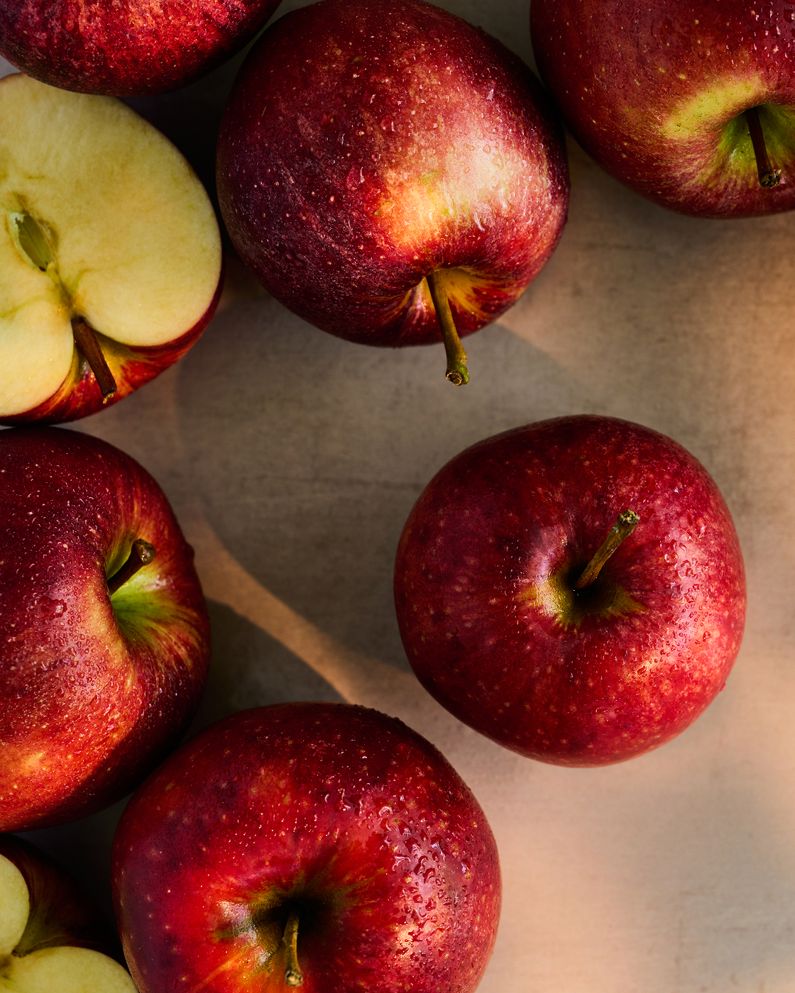 Several red apples and a sliced apple on a light surface.