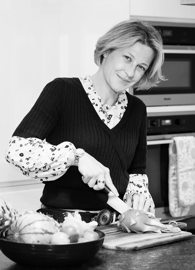 Person slicing a fruit in a kitchen with a bowl of fruits nearby.