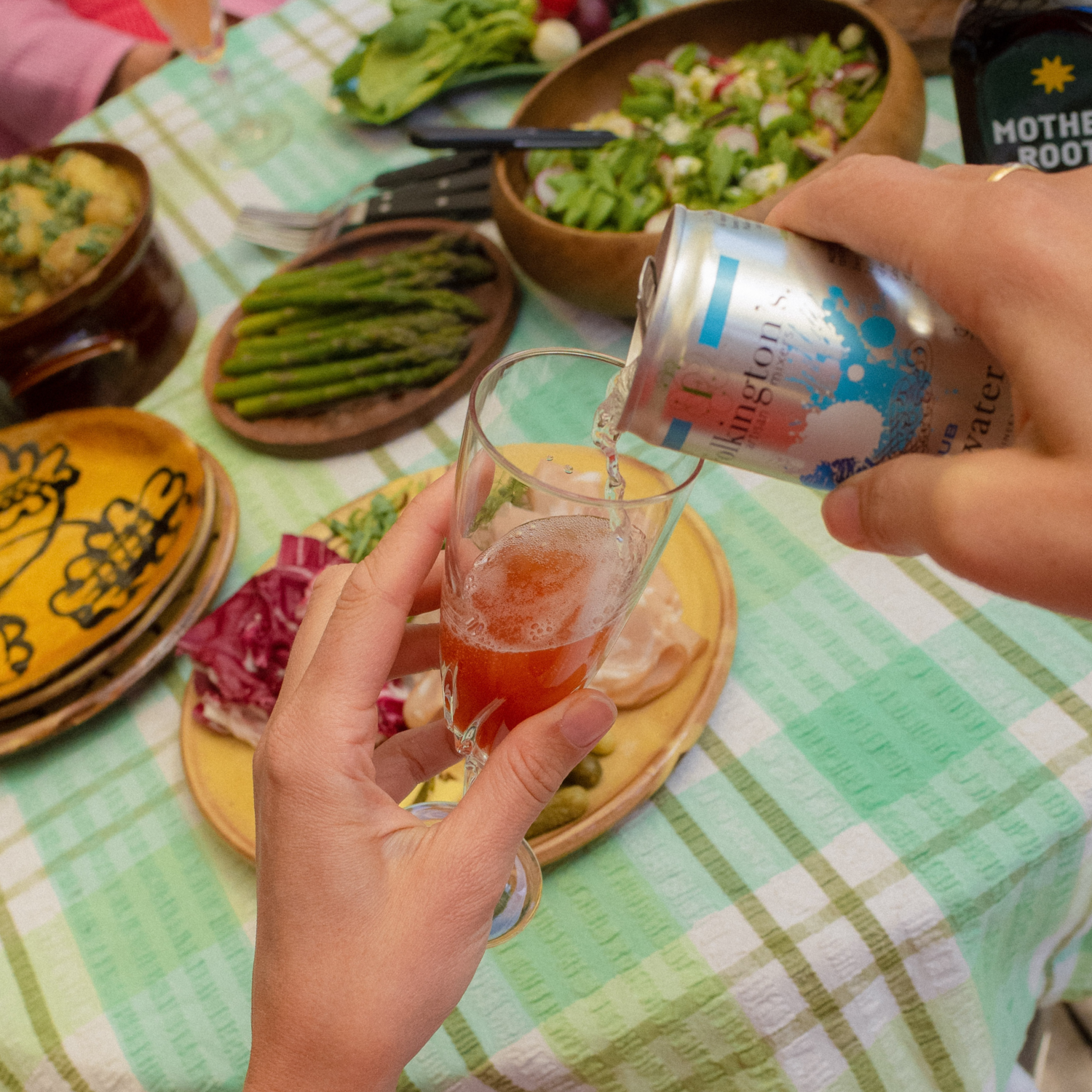 A person pours a drink into a salt-rimmed glass next to a bottle of Mother Root aperitif.