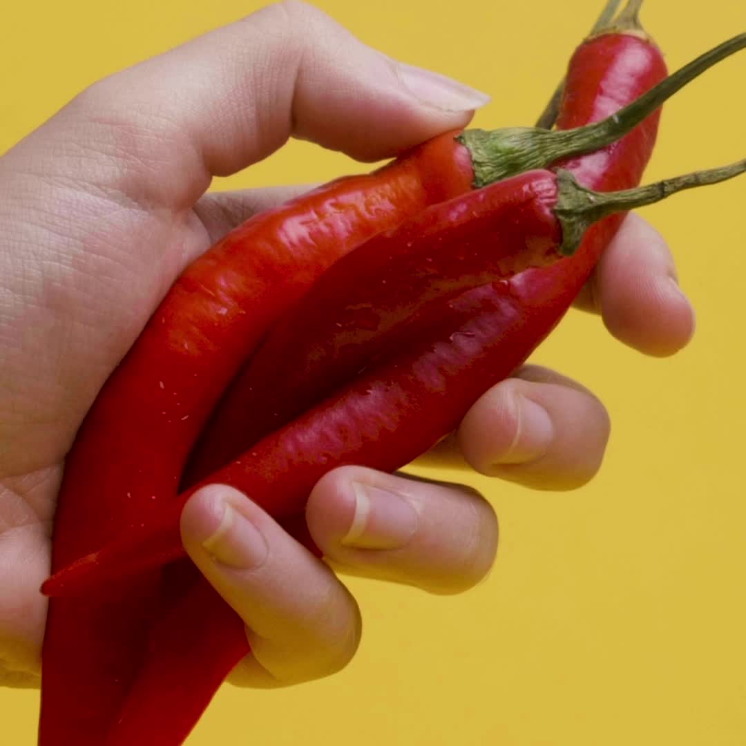 Hand holding three red chili peppers against a yellow background.