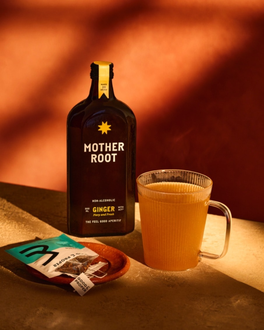 Bottle of Mother Root ginger drink with a glass and tea packet on a table.