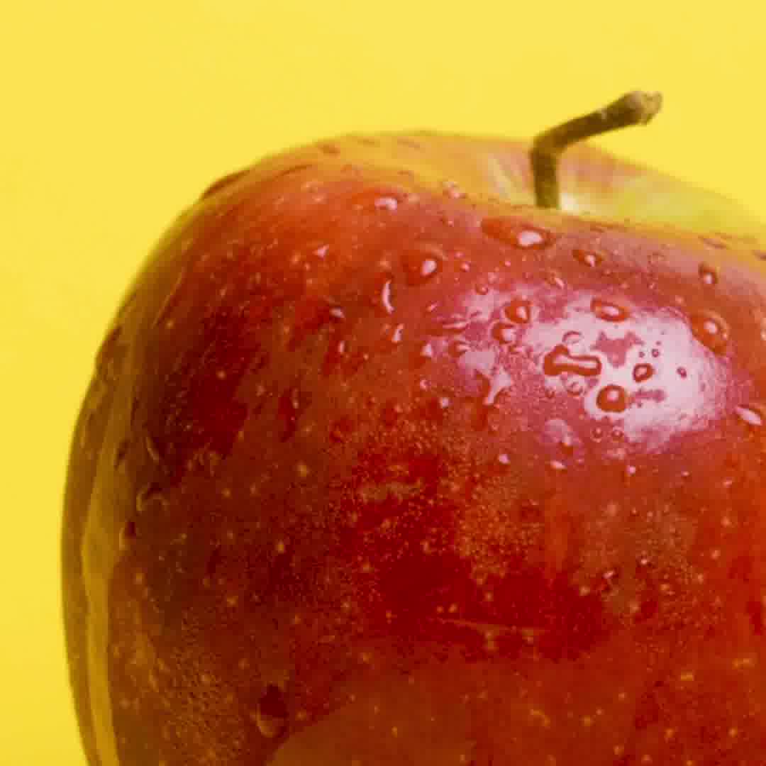Close-up of a red apple with water droplets on a yellow background.