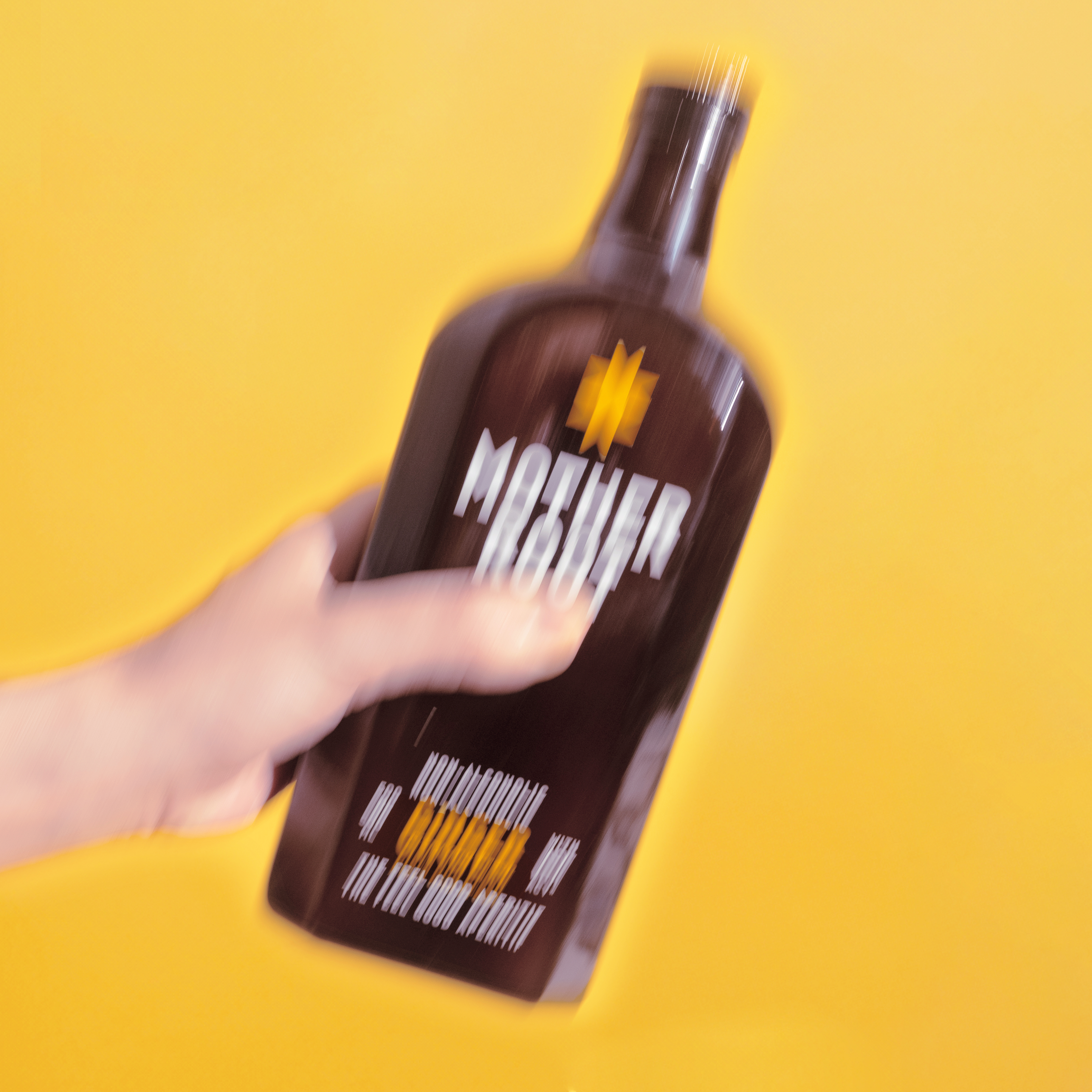 Blurry image of a hand holding a dark bottle against a yellow background.