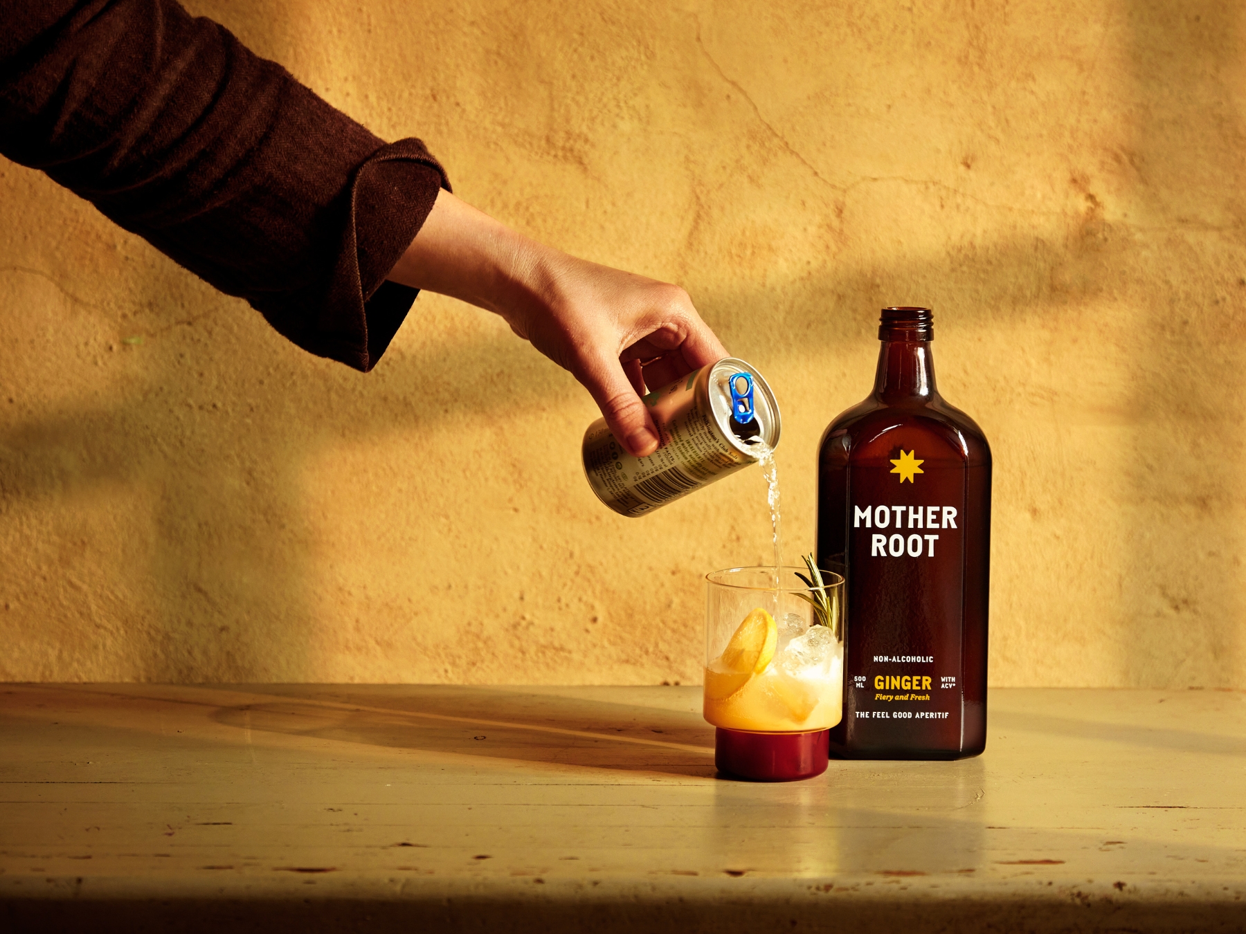 Hand pouring drink into glass beside Mother Root ginger bottle.