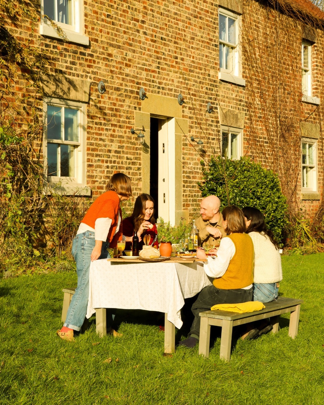 Group of people enjoying a meal at a table outside a brick house.
