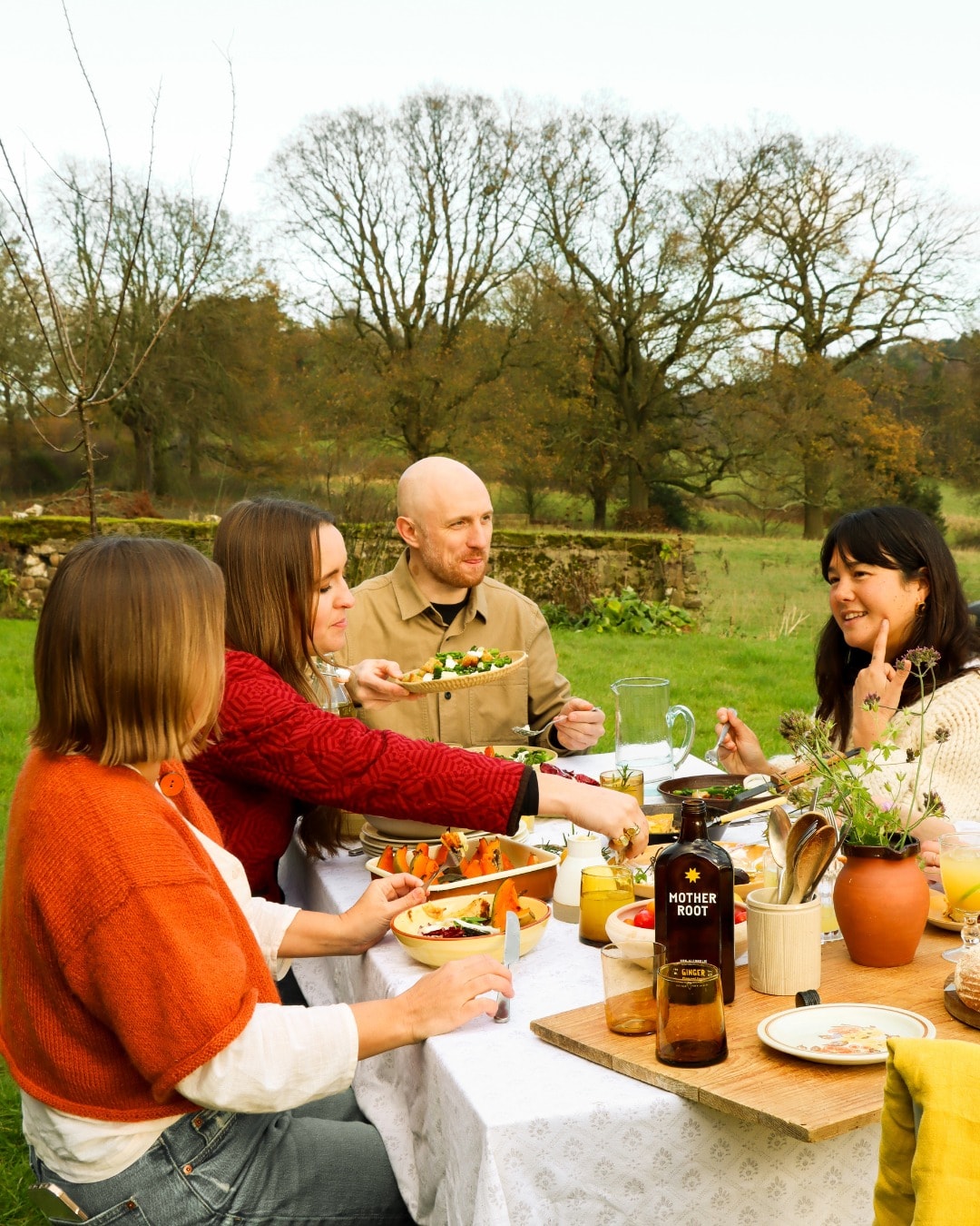 Four people enjoying a meal outdoors at a table with food and drinks.