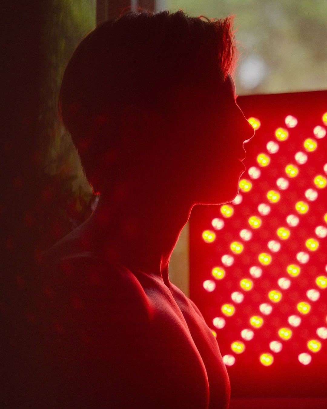 A silhouette of a person next to a red LED light panel.