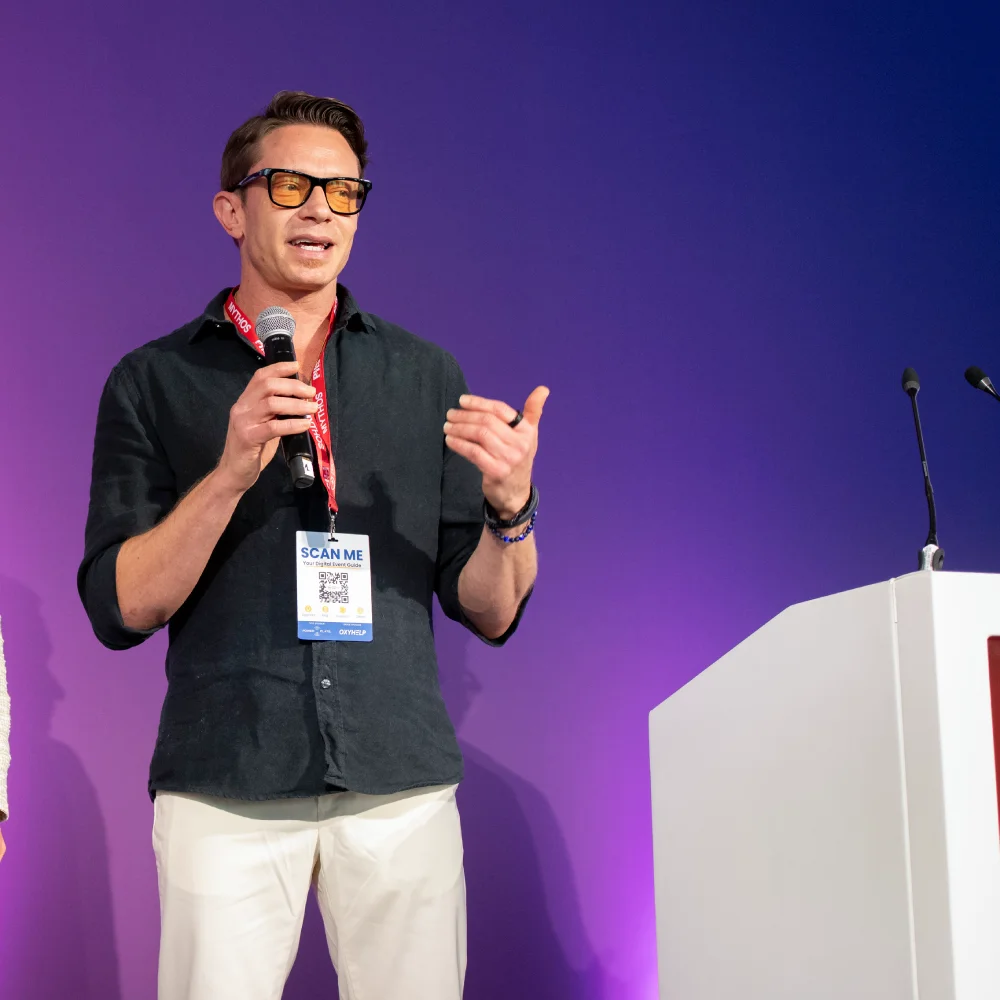 Person speaking on stage with a microphone and name badge.