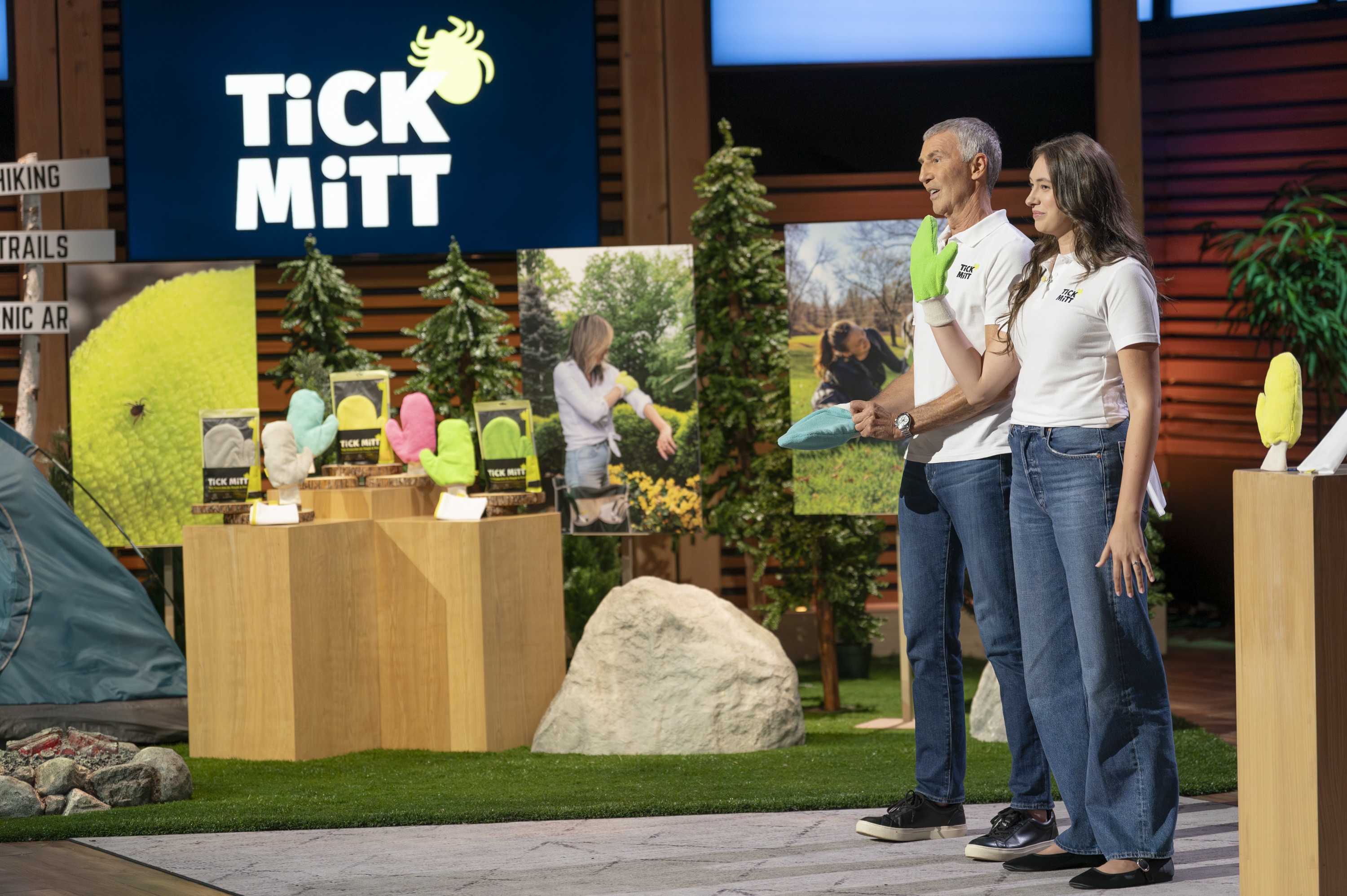 Two people presenting colorful mitts on a stage with a 'Tick Mitt' sign.