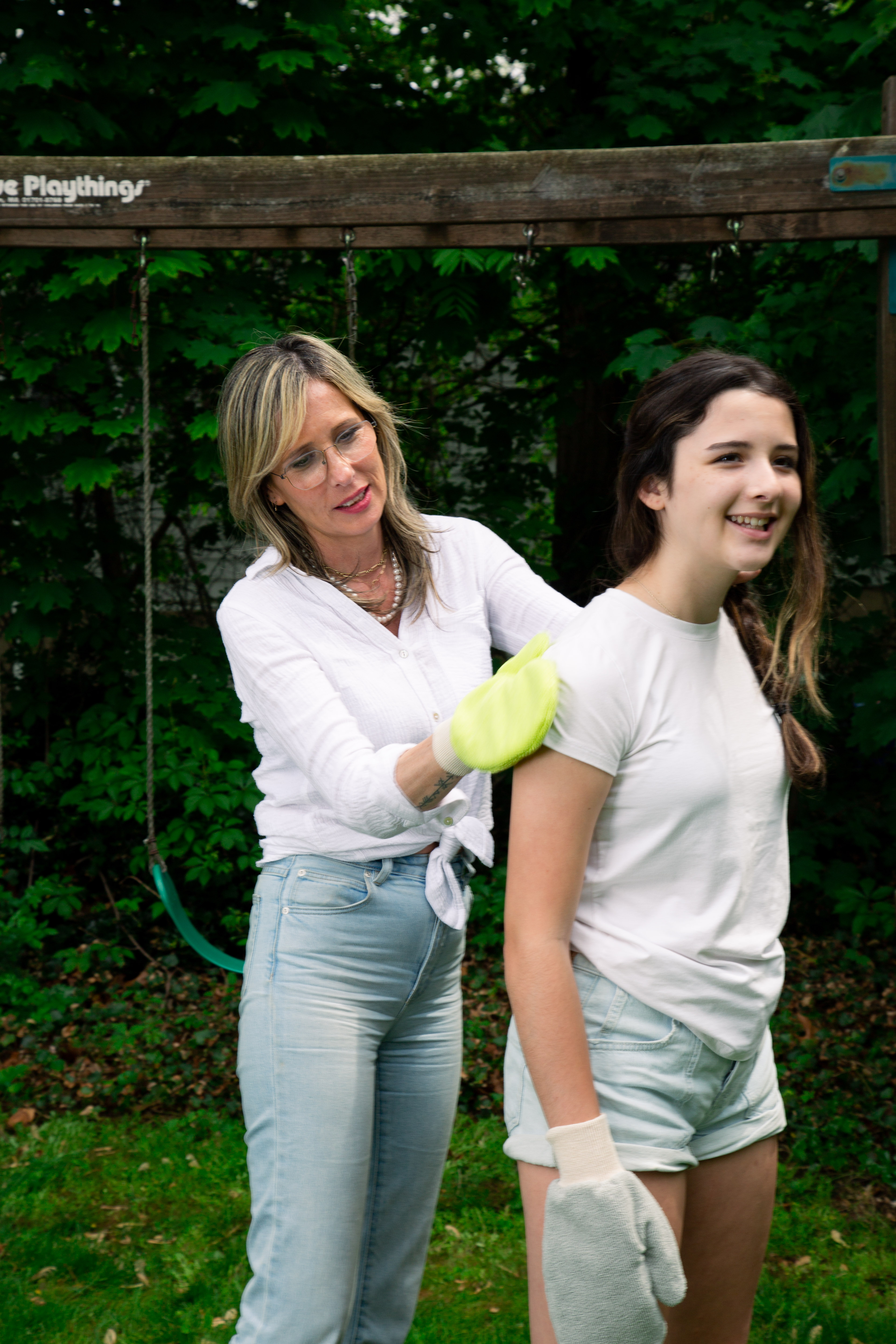 Two people in a garden, one wearing gloves, standing near a swing set.