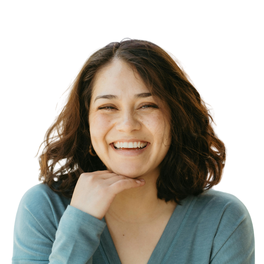 A woman with wavy brown hair smiles at the camera, resting her chin on her hand.