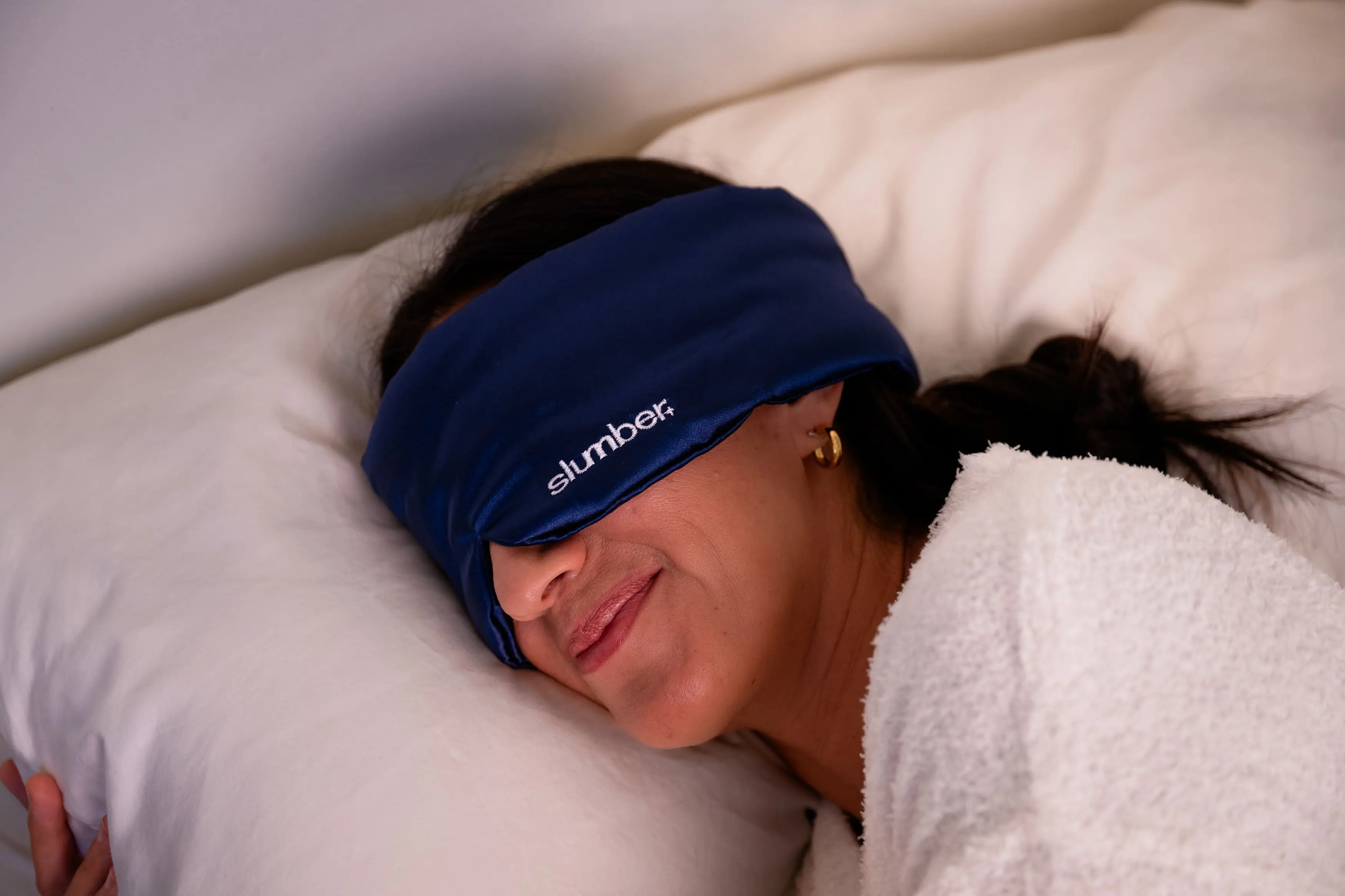 Person wearing a blue sleep mask labeled 'slumber' resting on a pillow.
