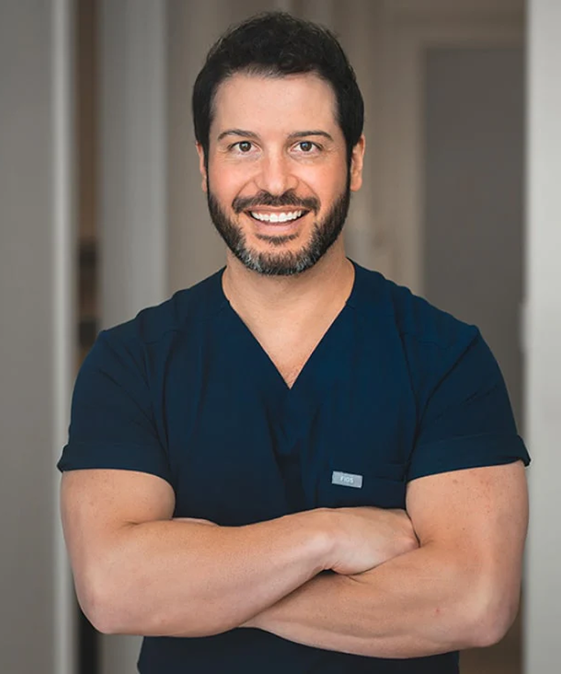 Smiling man with a beard in a dark blue shirt, arms crossed.