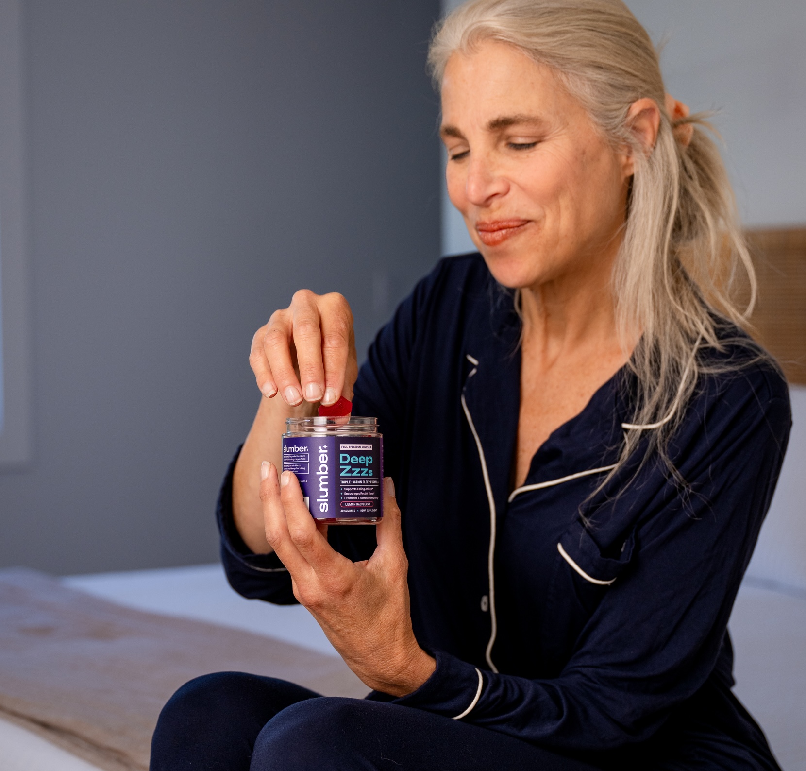 Person in pajamas holding a jar labeled 'Deep Zzzs' with a gummy in hand.
